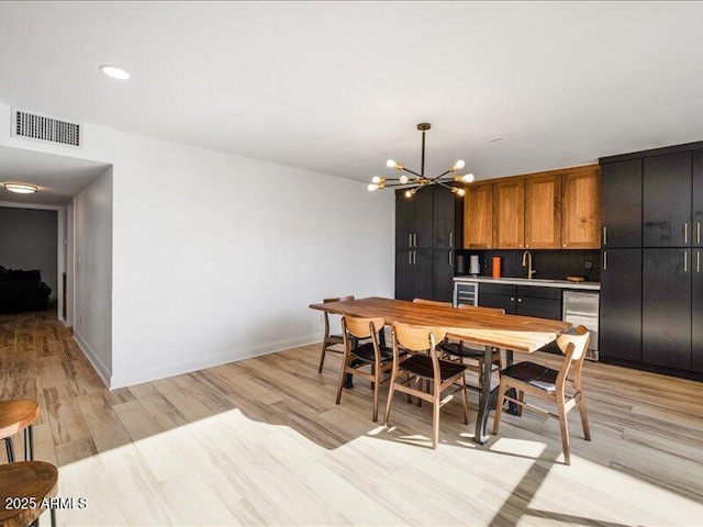 dining area with beverage cooler, a chandelier, sink, and light wood-type flooring