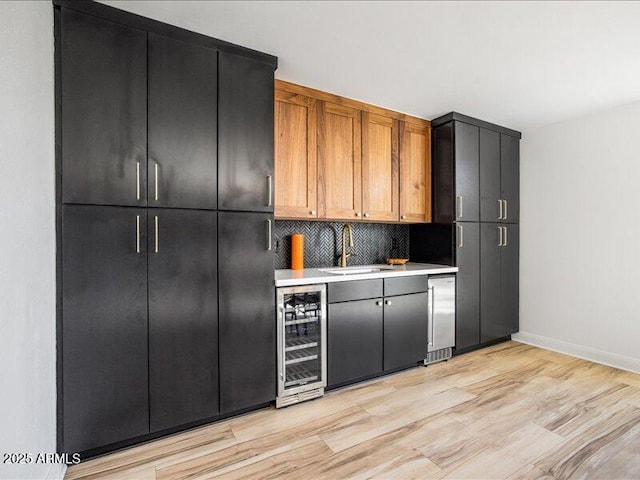 kitchen featuring wine cooler, light hardwood / wood-style floors, sink, and backsplash