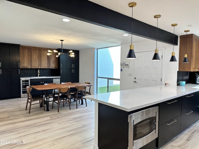 kitchen with backsplash, beam ceiling, stainless steel microwave, decorative light fixtures, and beverage cooler