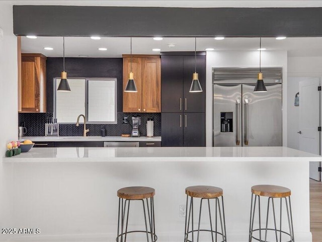 kitchen with pendant lighting, stainless steel built in refrigerator, sink, a kitchen bar, and decorative backsplash