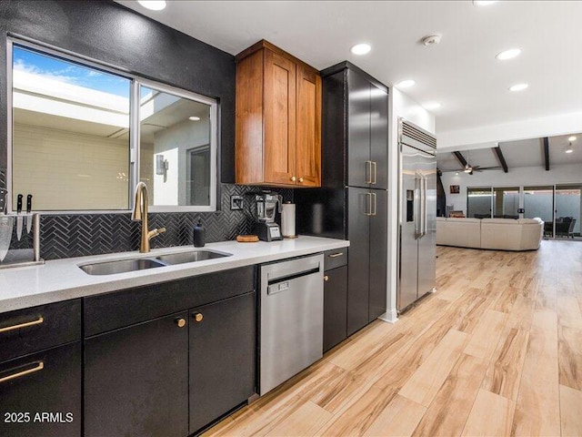 kitchen with sink, light wood-type flooring, backsplash, stainless steel appliances, and beam ceiling