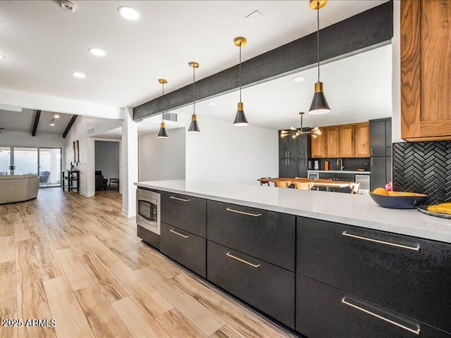 kitchen featuring stainless steel microwave, hanging light fixtures, backsplash, and vaulted ceiling with beams