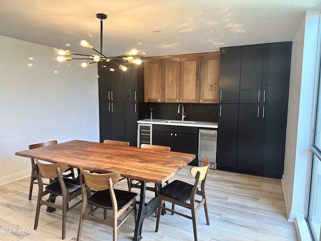 dining space featuring wine cooler, a notable chandelier, wet bar, and light wood-type flooring