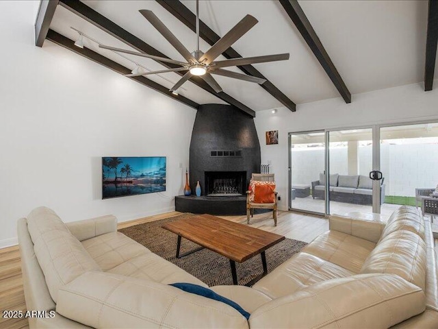 living room featuring ceiling fan, a large fireplace, light hardwood / wood-style flooring, and vaulted ceiling with beams