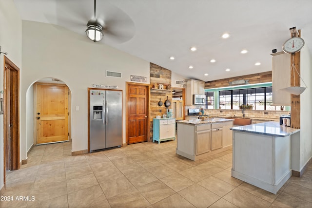 kitchen featuring ceiling fan, light stone counters, kitchen peninsula, stainless steel appliances, and a center island