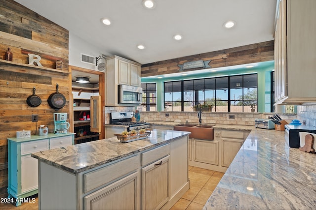 kitchen with light stone counters, a center island, sink, wood walls, and stainless steel appliances