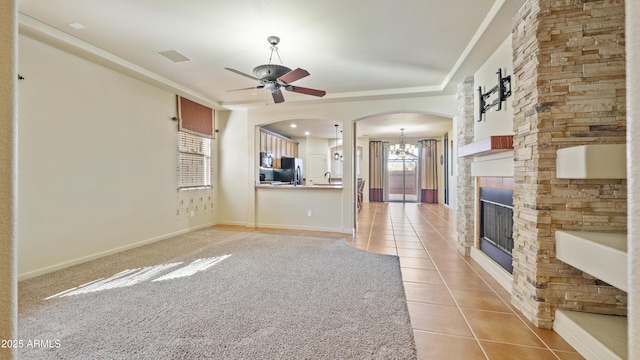 unfurnished living room featuring light tile patterned floors, visible vents, arched walkways, a stone fireplace, and ceiling fan with notable chandelier