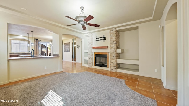 unfurnished living room featuring a ceiling fan, a tray ceiling, tile patterned flooring, and a stone fireplace