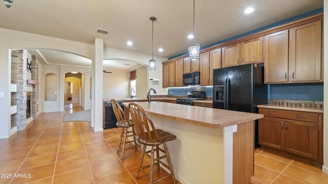 kitchen with arched walkways, light tile patterned floors, visible vents, a kitchen breakfast bar, and black appliances