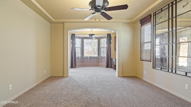 carpeted spare room featuring baseboards, a tray ceiling, and arched walkways