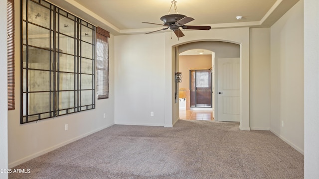 unfurnished room with arched walkways, carpet flooring, a ceiling fan, baseboards, and a tray ceiling