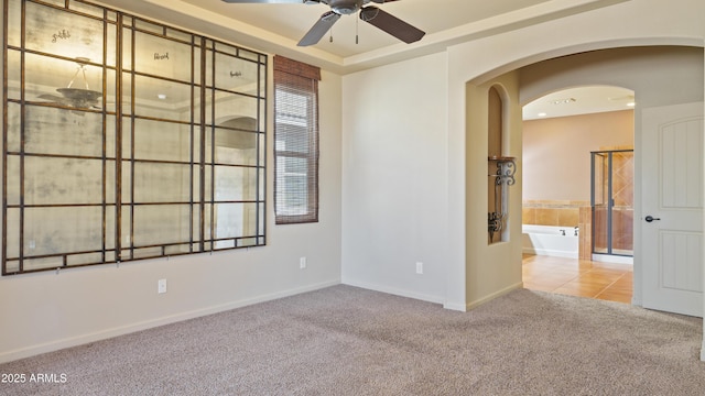 empty room featuring arched walkways, a raised ceiling, a ceiling fan, baseboards, and carpet