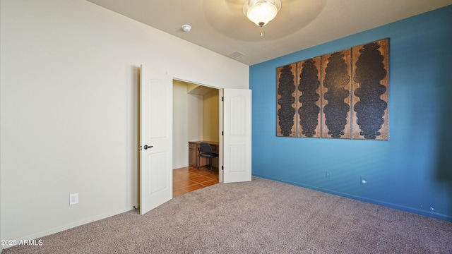 unfurnished bedroom featuring carpet floors, visible vents, a ceiling fan, baseboards, and tile patterned floors