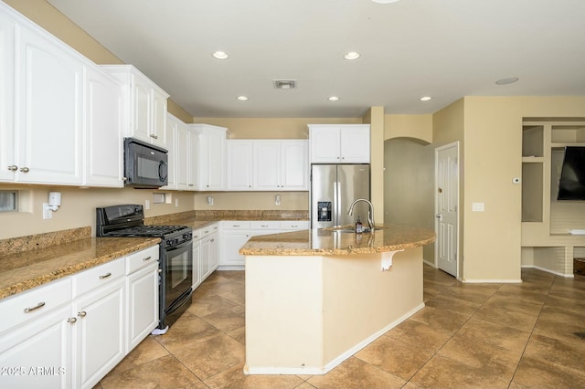 kitchen featuring white cabinets, light stone countertops, a kitchen island with sink, and black appliances