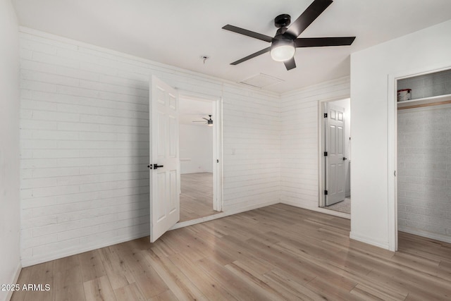 unfurnished bedroom featuring light wood-type flooring, a closet, ceiling fan, and brick wall