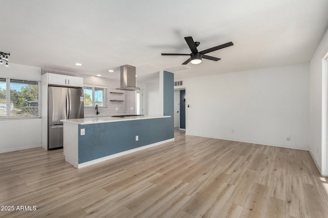 kitchen with white cabinetry, stainless steel appliances, tasteful backsplash, island range hood, and light wood-type flooring