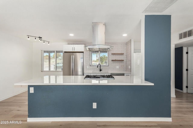 kitchen featuring island range hood, light hardwood / wood-style flooring, stainless steel appliances, decorative backsplash, and white cabinets