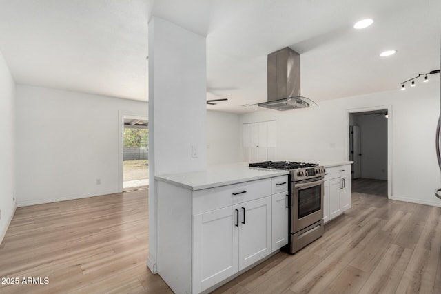 kitchen featuring stainless steel gas range, island range hood, ceiling fan, light hardwood / wood-style floors, and white cabinets