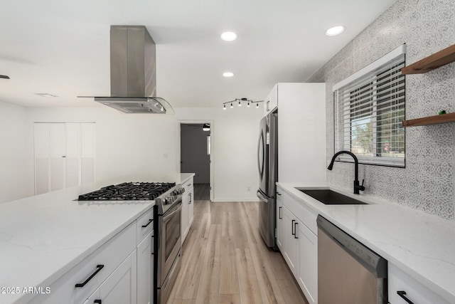 kitchen with island range hood, stainless steel appliances, sink, and white cabinets