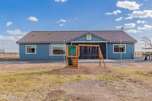 back of property with a tile roof, a playground, and fence