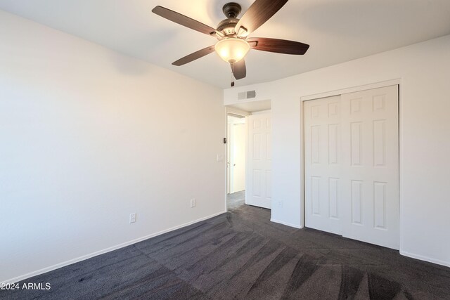 unfurnished bedroom with a closet, dark carpet, and ceiling fan