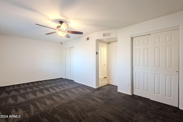 unfurnished bedroom with ceiling fan, dark colored carpet, and two closets