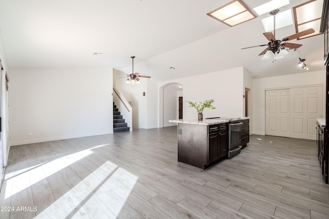 kitchen featuring electric stove, a center island with sink, vaulted ceiling with skylight, and light hardwood / wood-style floors