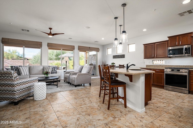 kitchen featuring pendant lighting, sink, appliances with stainless steel finishes, a kitchen bar, and a center island with sink