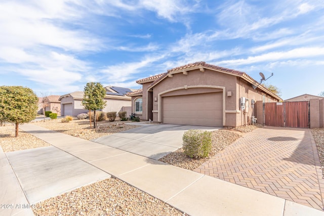 mediterranean / spanish house with a garage, driveway, a tiled roof, a gate, and stucco siding