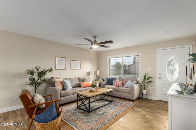 living area featuring light wood finished floors, a ceiling fan, and baseboards