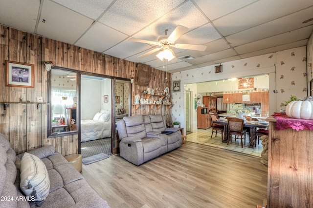 living room with a paneled ceiling, ceiling fan, hardwood / wood-style floors, and wooden walls