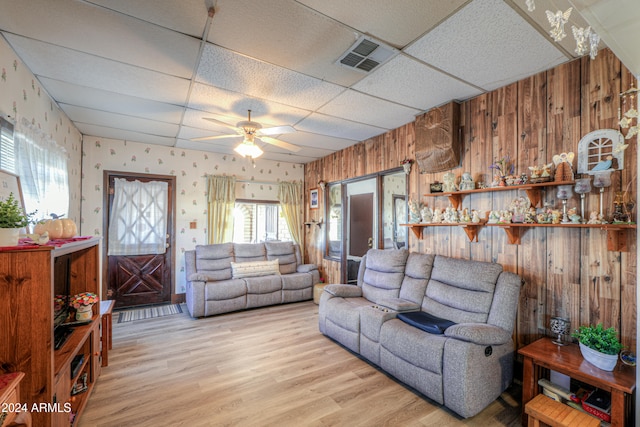 living room with a paneled ceiling, wood walls, ceiling fan, and light hardwood / wood-style floors