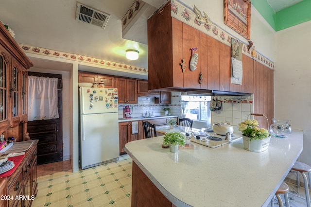 kitchen featuring kitchen peninsula, refrigerator, tasteful backsplash, sink, and a breakfast bar area