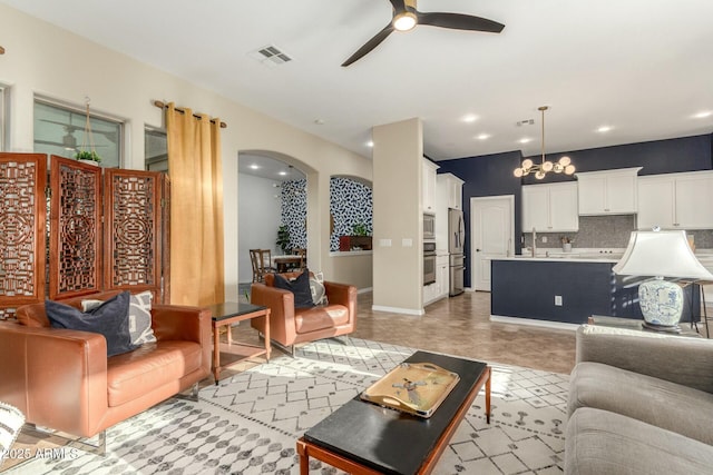 living area with arched walkways, recessed lighting, ceiling fan with notable chandelier, visible vents, and baseboards