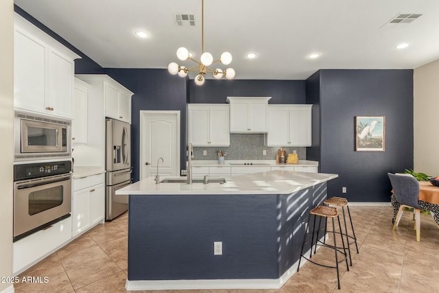 kitchen with a large island, stainless steel appliances, light countertops, visible vents, and a sink