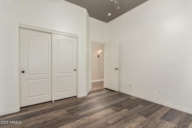 unfurnished bedroom with dark wood-style floors, baseboards, and a closet