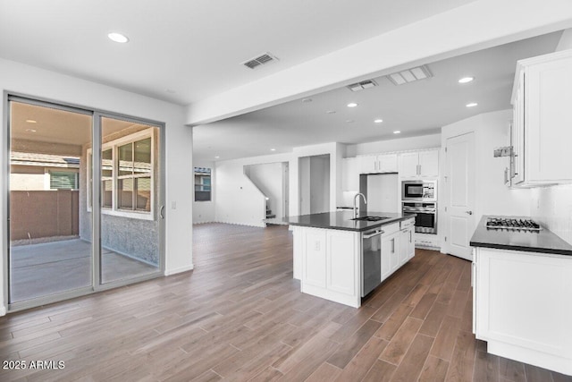 kitchen with wood finished floors, a sink, visible vents, appliances with stainless steel finishes, and dark countertops