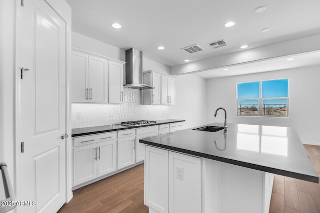 kitchen with stainless steel gas cooktop, visible vents, a sink, wood finished floors, and wall chimney exhaust hood