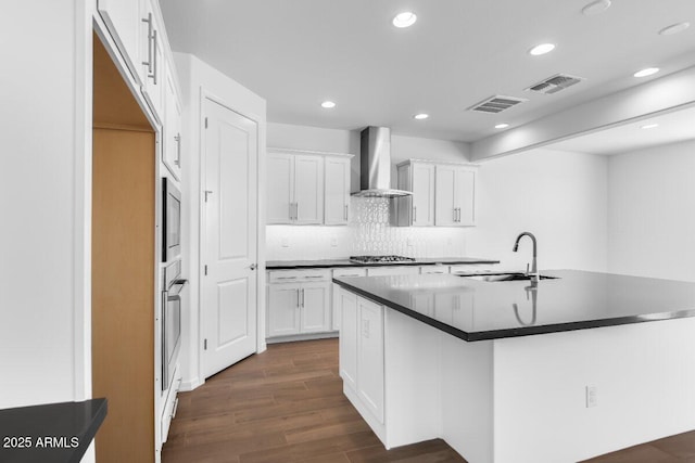 kitchen with dark countertops, visible vents, a sink, and wall chimney range hood