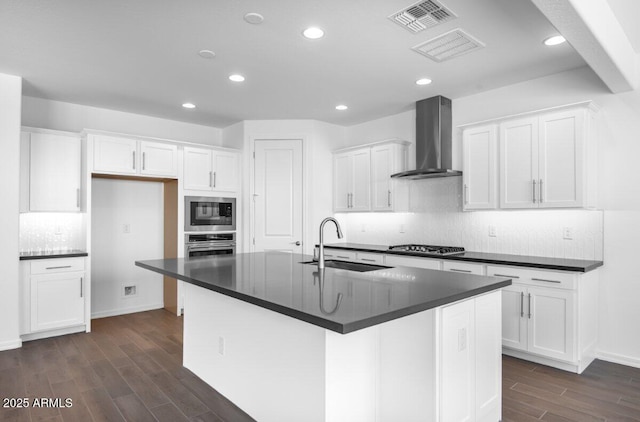 kitchen featuring stainless steel appliances, dark wood-type flooring, a sink, wall chimney range hood, and dark countertops