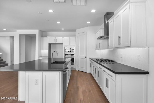 kitchen featuring wall chimney range hood, dark countertops, a sink, and appliances with stainless steel finishes