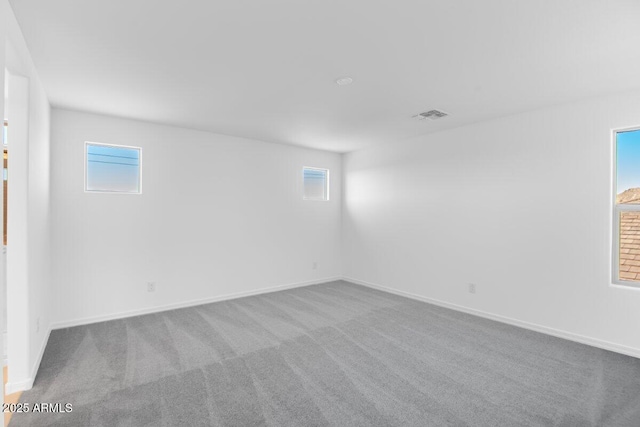 carpeted spare room with baseboards, visible vents, and a healthy amount of sunlight