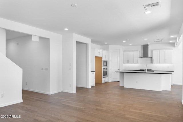 kitchen with light wood-style flooring, a sink, visible vents, wall chimney range hood, and dark countertops