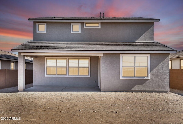 back of property at dusk featuring a patio area, fence, a tile roof, and stucco siding