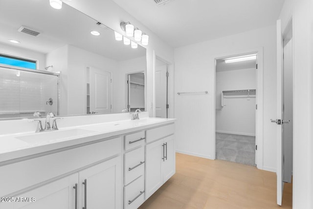 full bathroom with a spacious closet, a sink, visible vents, and a shower stall