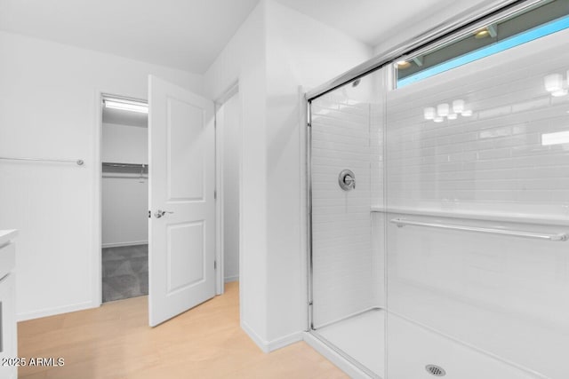 full bathroom with a walk in closet, a shower stall, vanity, wood finished floors, and baseboards