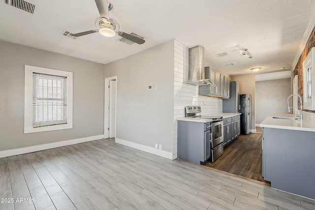 kitchen featuring stainless steel range with electric stovetop, a sink, wall chimney range hood, light countertops, and ceiling fan