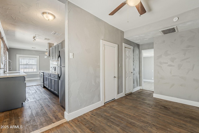 kitchen featuring a sink, appliances with stainless steel finishes, a ceiling fan, dark wood-style flooring, and gray cabinetry