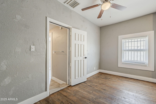 unfurnished bedroom with wood-type flooring, baseboards, a textured wall, and ceiling fan
