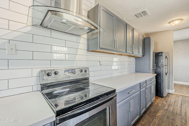 kitchen featuring stainless steel electric range oven, wall chimney range hood, dark wood finished floors, gray cabinetry, and tasteful backsplash